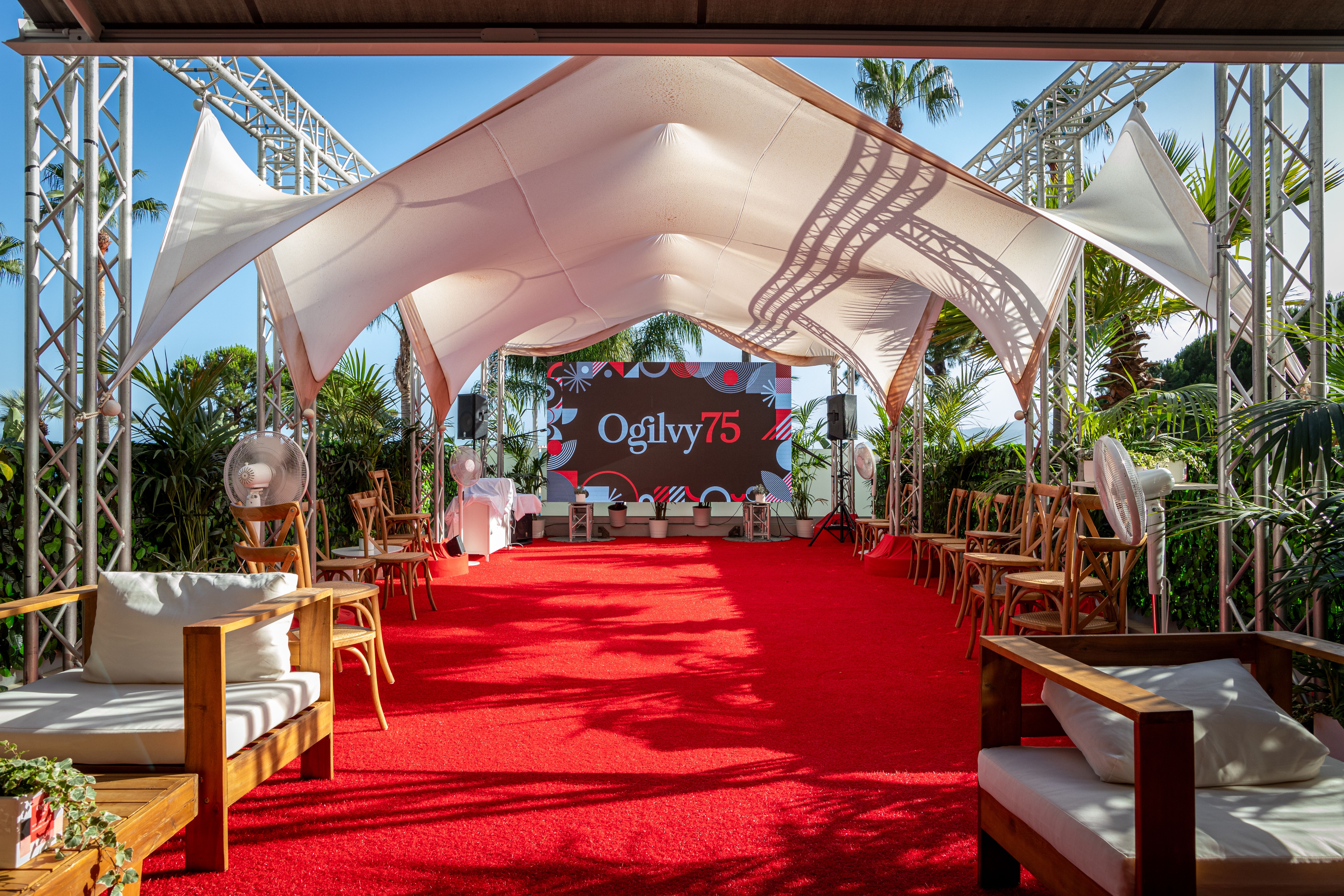 Event installation in Cannes before guests arrive, with a screen and stage under an outdoor structure